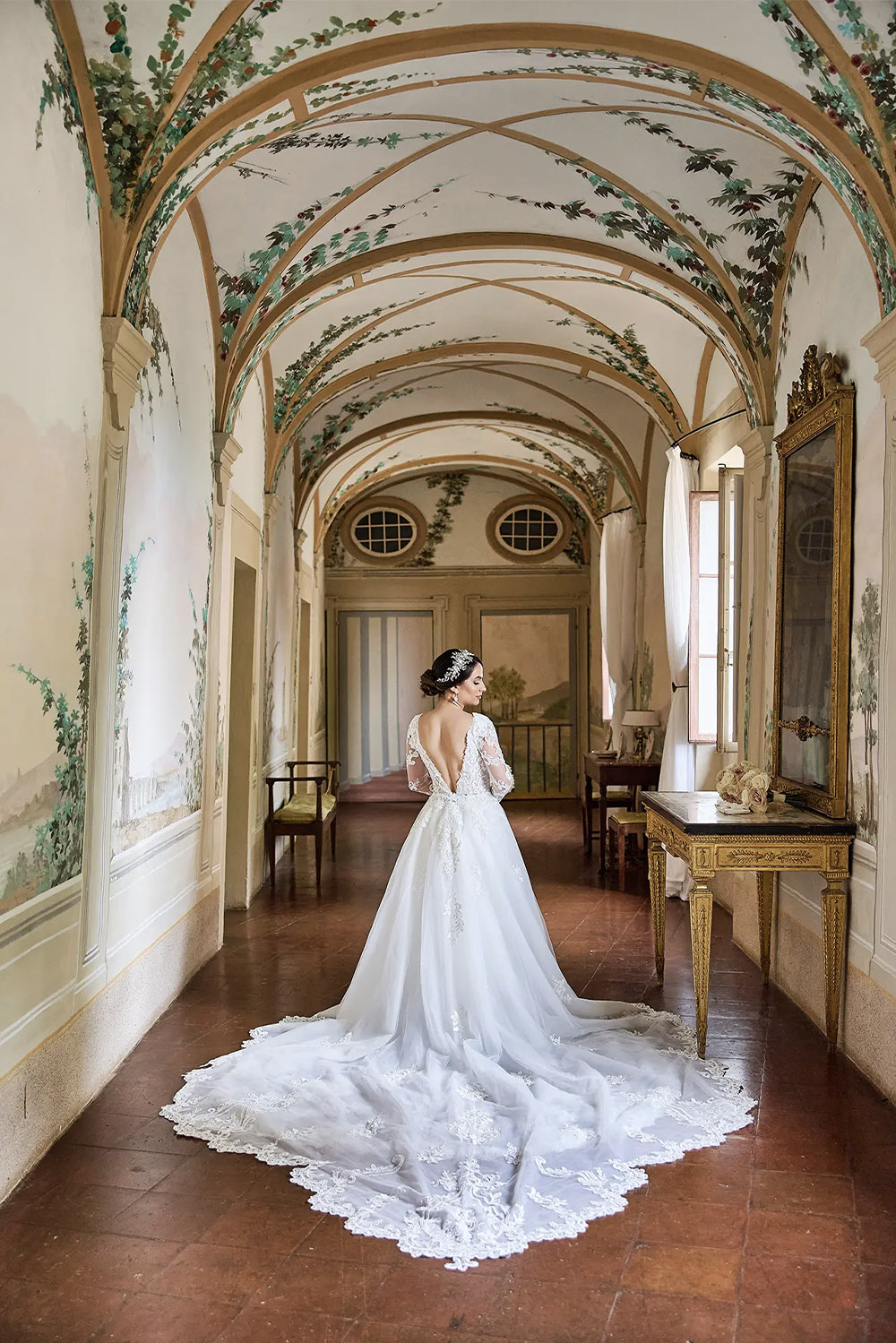 An editorial bridal portrait at Castello di Celsa in Tuscany, Italy, featuring a bride standing beneath a beautifully frescoed ceiling in one of the castle's historic rooms.