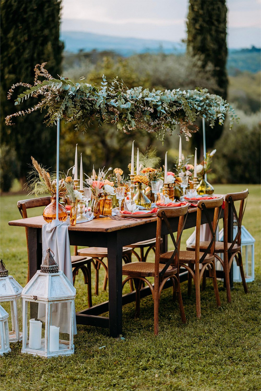 Borgo Iesolana, Tuscany, Italy — an elegant outdoor wedding reception table decorated with lush greenery, warm-toned florals, candles, and vintage glassware in an editorial style.