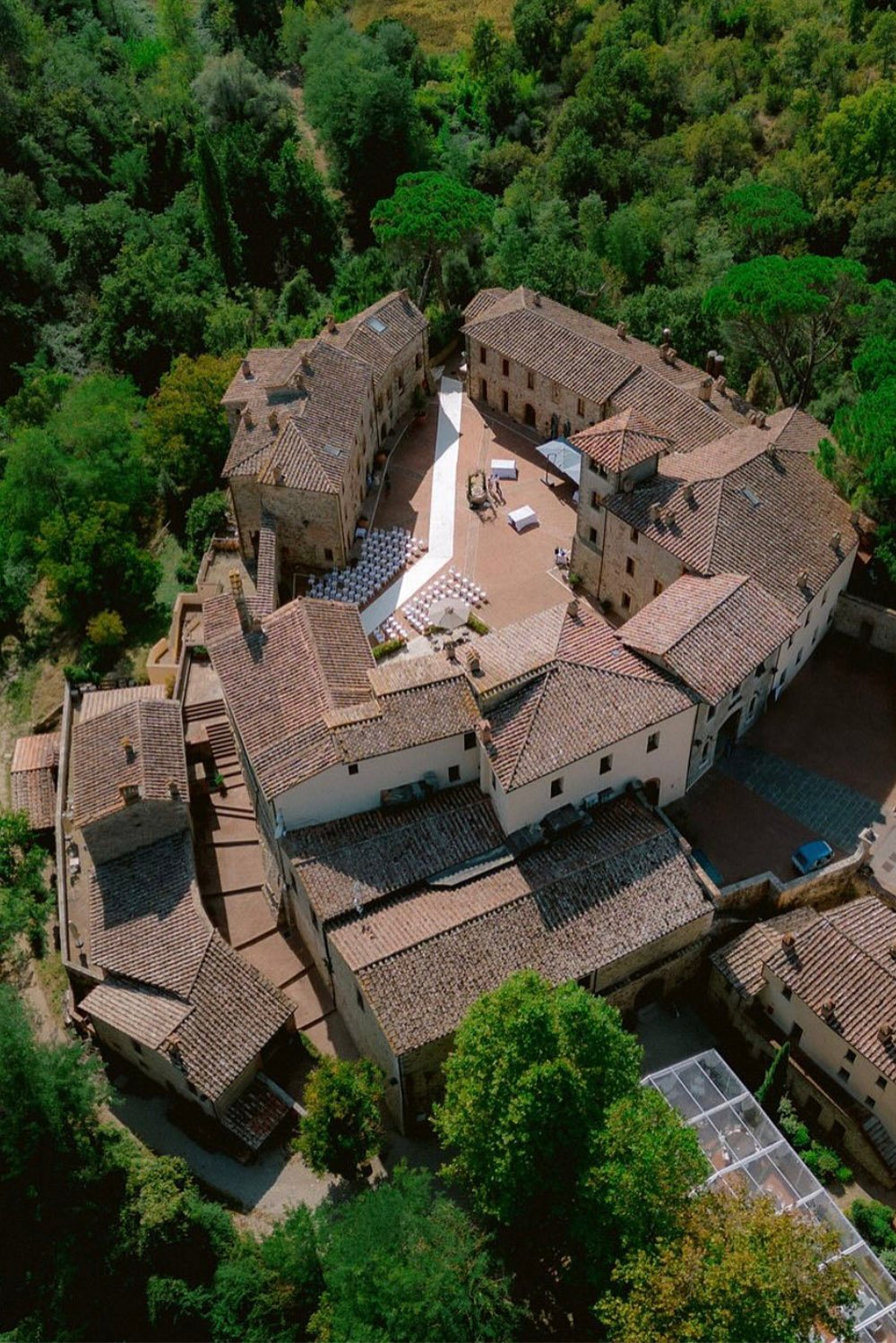 Castel Monastero, Tuscany, Italy — an aerial view of the historic stone buildings and central courtyard surrounded by lush Tuscan woodland, photographed in an elegant editorial style.