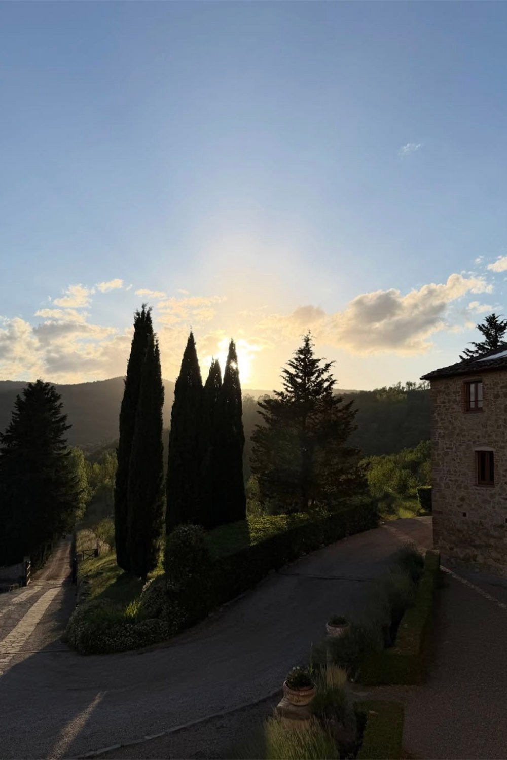 Il Verreno Resort, Tuscany, Italy — A golden-hour view of Il Verreno Resort framed by tall cypress trees and Tuscan hills, creating a cinematic editorial atmosphere.