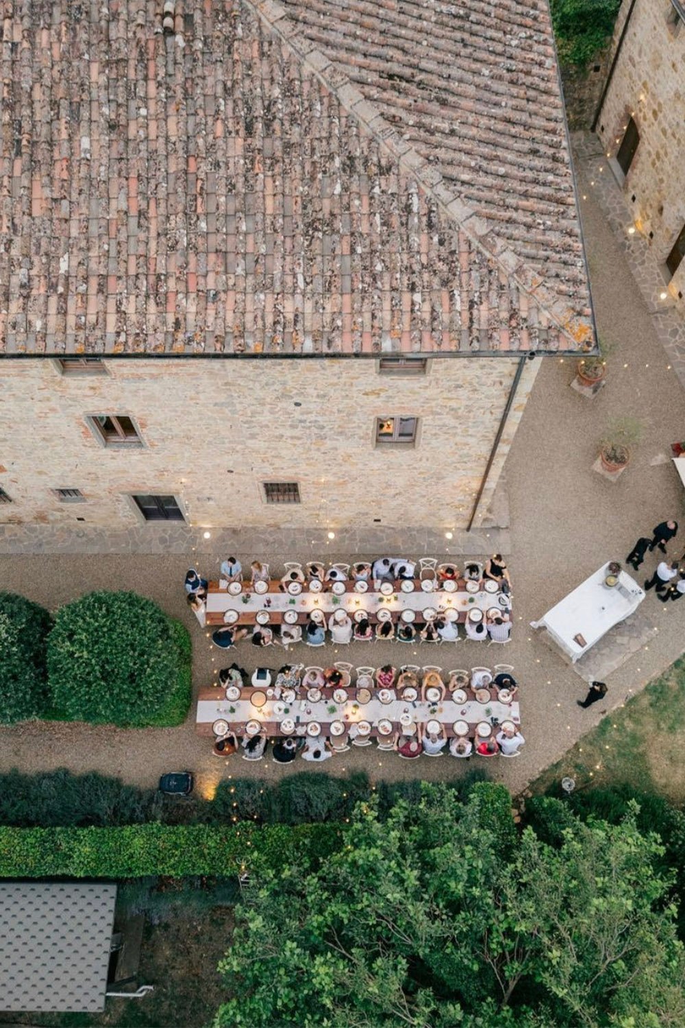 Il Verreno Resort, Tuscany, Italy — An aerial view of an intimate wedding dinner at Il Verreno Resort, with long candlelit tables arranged in the historic stone courtyard in an elegant editorial style.