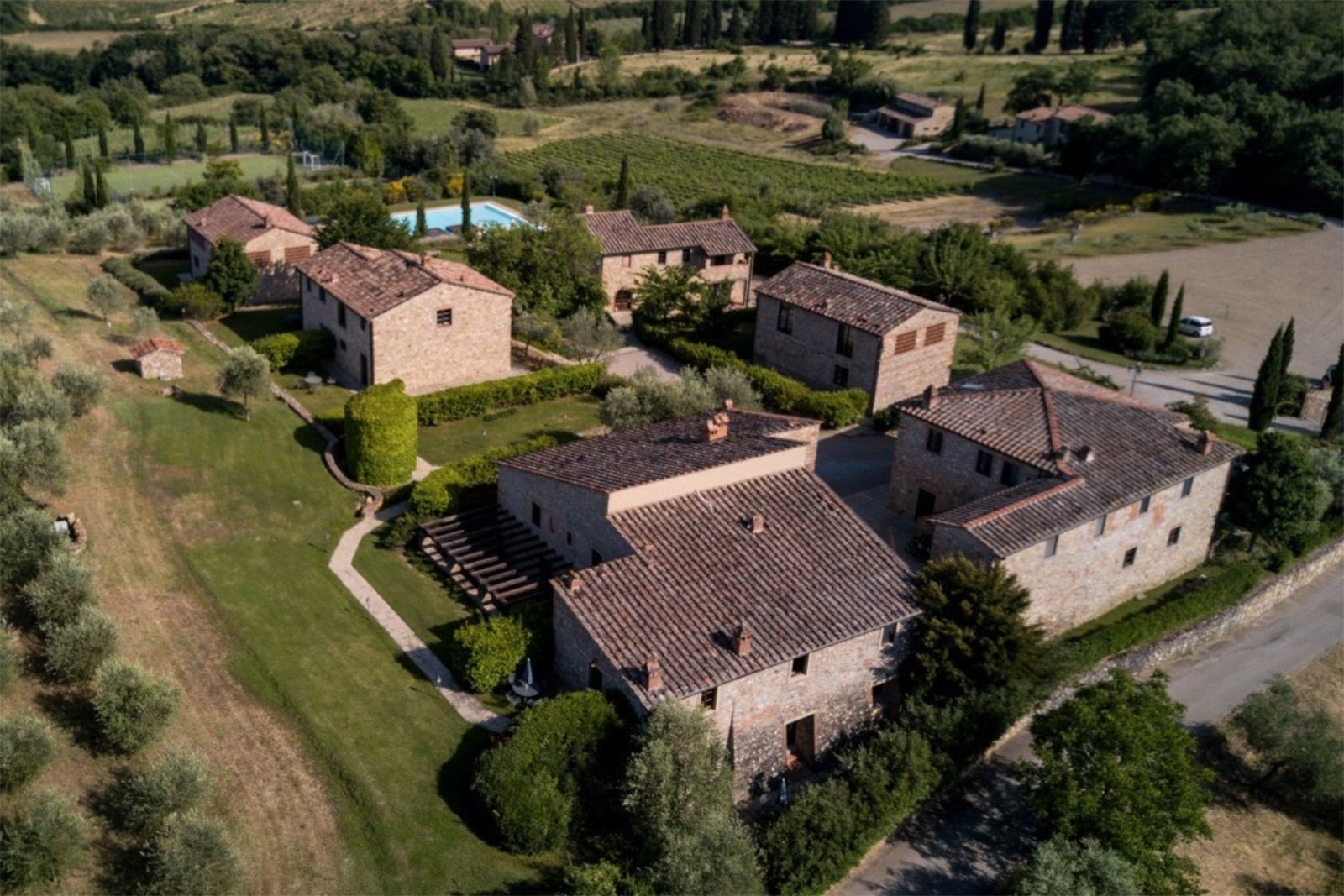 Poggio Cennina Resort: Aerial view of Poggio Cennina Resort in Tuscany, Italy, surrounded by rolling countryside, olive trees, vineyards, and traditional stone buildings in an elegant editorial style.